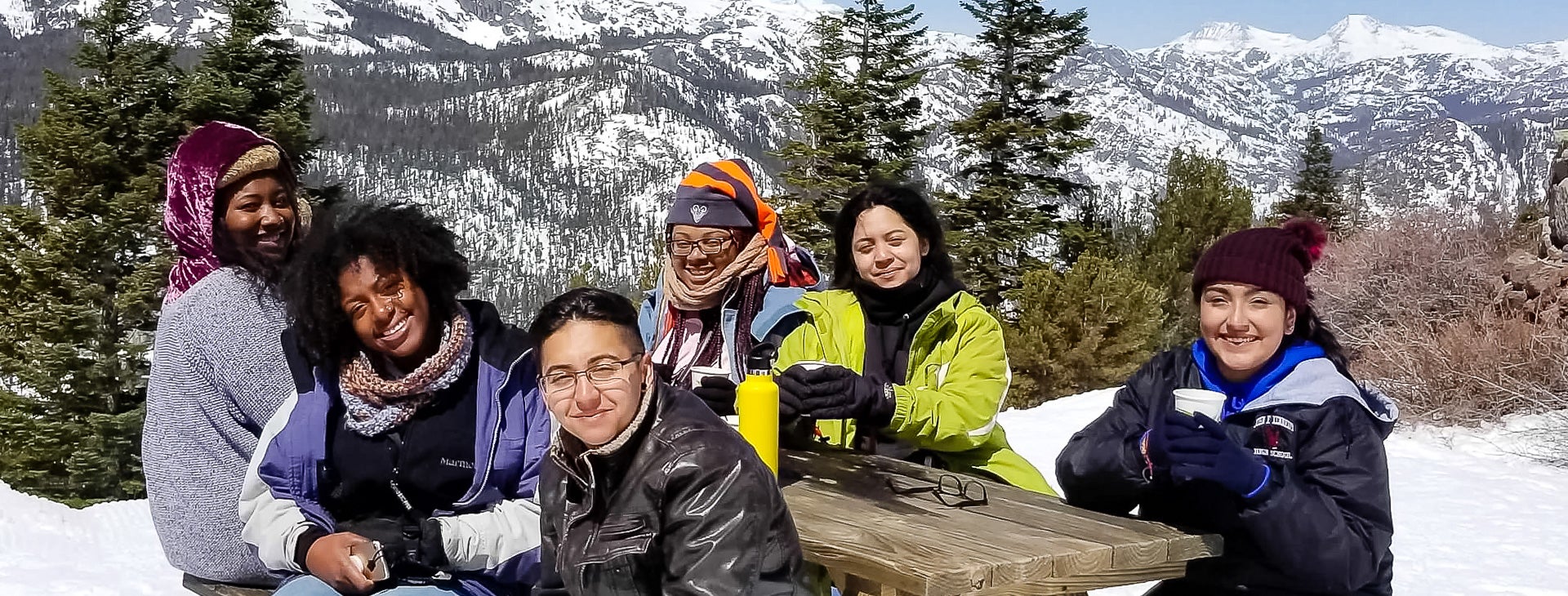 Photo of Foster Youth students at a picnic tables in the snow covered mountains.