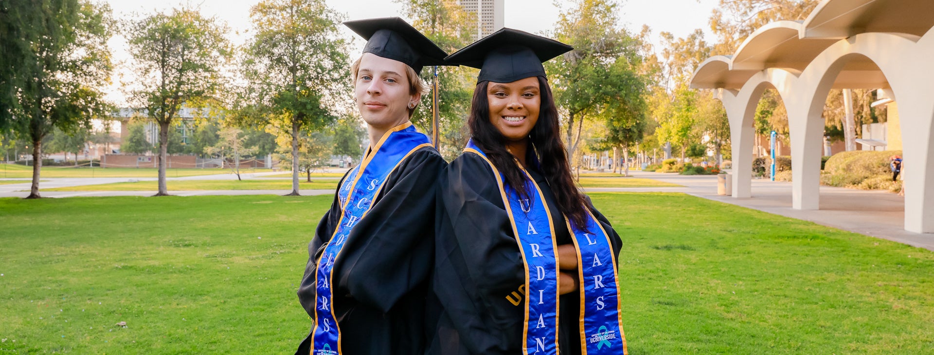 Photo of two Guardian Scholars graduates posing by the Rivera Library on the UCR campus.